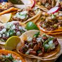 Assortment Of Delicious Authentic Tacos, Birria, Carne Asada, Adobada, Cabeza And Chicharone, Arranged With Lime Slices, Onion, And Roasted Chili Pepper
