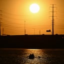 El sol se pone detrás de las líneas eléctricas mientras la gente rema en Tempe Town Lake durante una ola de calor récord en Tempe, Arizona, el 18 de julio de 2023.