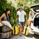 Wide shot of family preparing to load rental car with luggage while on vacation