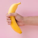 Male hand holding a banana isolated on pink background.