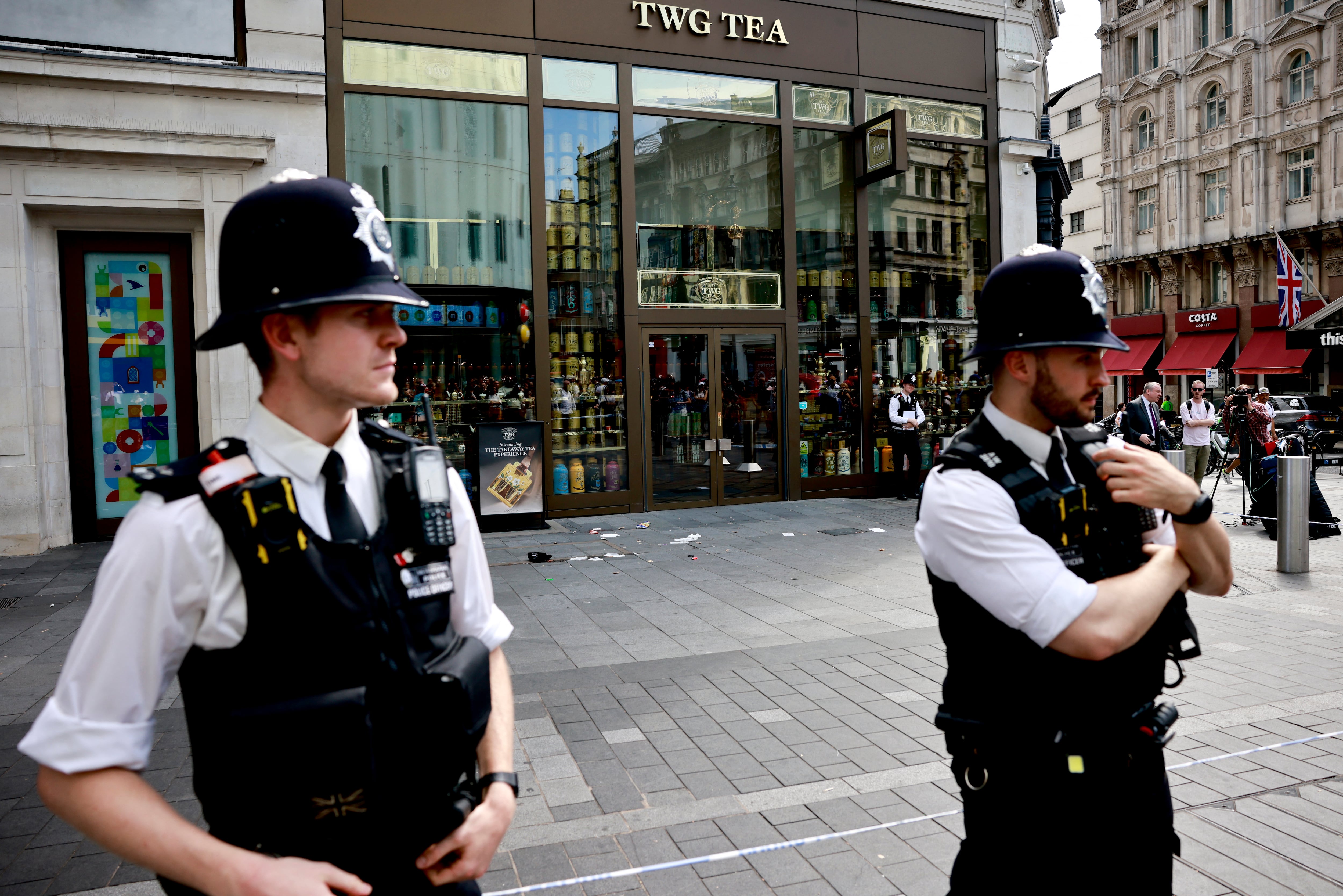 Una fotografía tomada el 12 de agosto de 2024 muestra a agentes de policía de pie junto a una zona acordonada en Leicester Square, Londres. Una mujer y una niña de 11 años fueron hospitalizadas el 12 de agosto después de ser apuñaladas en la famosa Leicester Square del centro de Londres, dijo la policía, añadiendo que un hombre había sido arrestado. (Foto de BENJAMIN CREMEL / AFP)