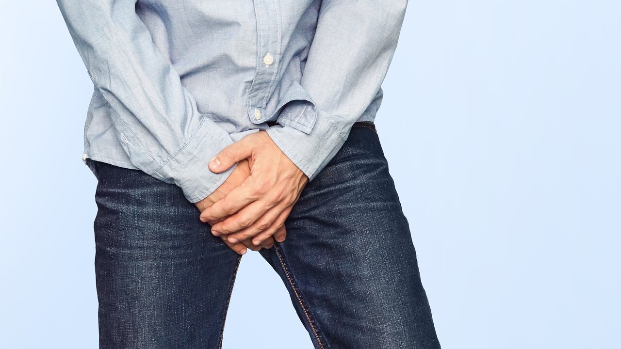 Close up of a man with hands holding his crotch on a light blue background. Urinary incontinence. Men's health. The pain from the blow in groin.