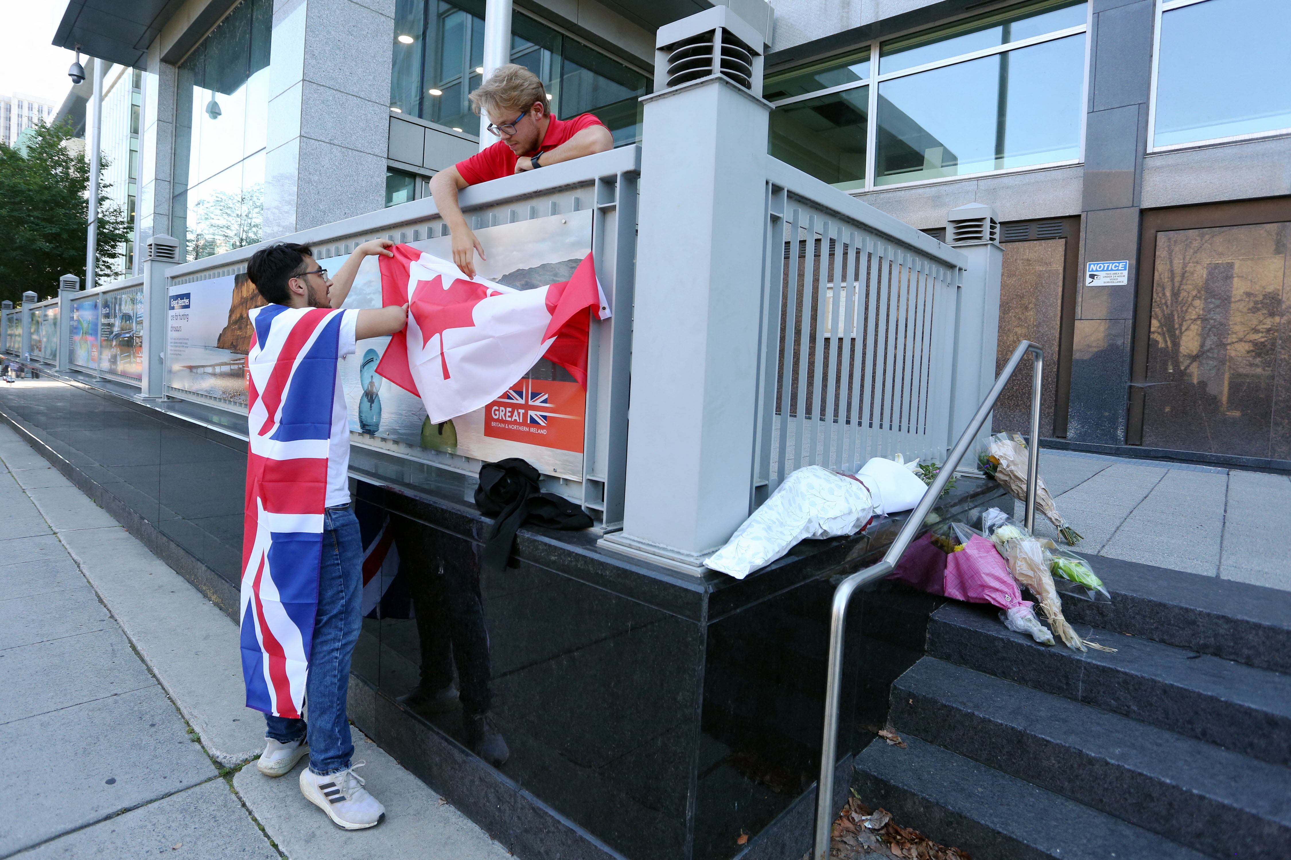 La doliente Eissa Saddozai (L) y Aidan Osadchuk colocan una bandera canadiense en los escalones de la Alta Comisión Británica después de la muerte de la Reina Isabel II de Gran Bretaña el 8 de septiembre de 2022 en Ottawa, Canadá. - La reina Isabel II, la monarca con más años de servicio en la historia británica y un ícono instantáneamente reconocible para miles de millones de personas en todo el mundo, murió a los 96 años, dijo el Palacio de Buckingham. (Foto de Dave Chan / AFP)