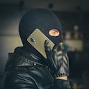 Young adult in black clothes with hidden face. Ill-intended fraudster uses mobile. Fraudster calls. Mobile racket. Hacker hijacks by phone. Cellphone account fraud. Scam