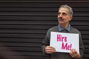 Senior asian man standing looking away from the camera while holding a hire me sign.