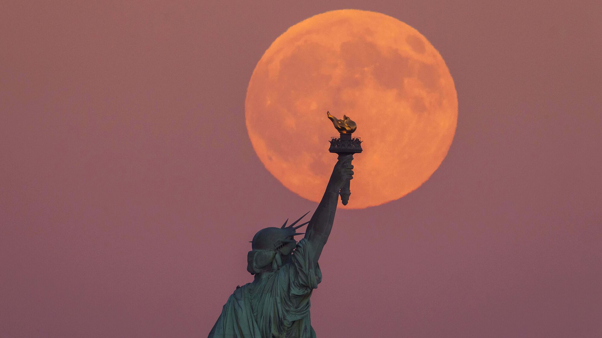 La Superluna de la Cosecha se levanta detrás de la Estatua de la Libertad y el horizonte de Brooklyn en Jersey City, Nueva Jersey. Lunes 6 de octubre de 2025.