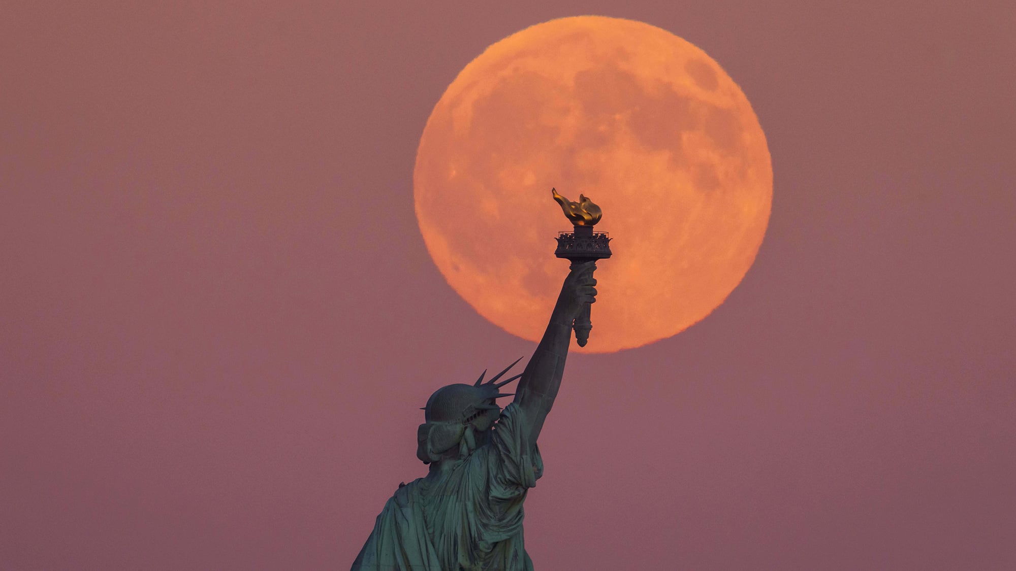 La Superluna de la Cosecha se levanta detrás de la Estatua de la Libertad y el horizonte de Brooklyn en Jersey City, Nueva Jersey. Lunes 6 de octubre de 2025.