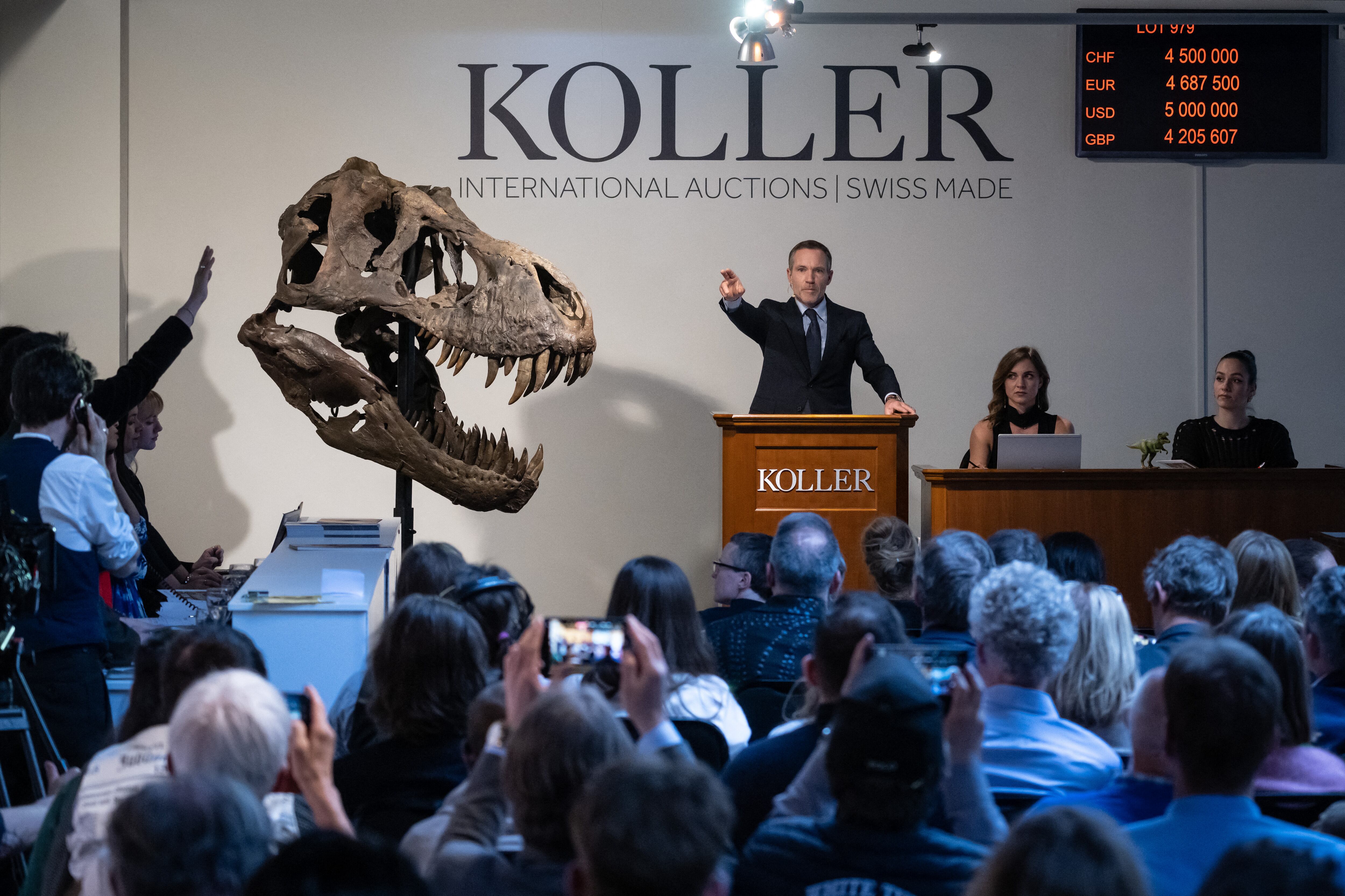 El director de la casa de subastas Koller, Cyril Koller (C), hace un gesto junto al cráneo de la 'Trinidad' durante la venta del esqueleto del Tyrannosaurus-Rex (T-Rex) por la casa de subastas Koller en Zúrich