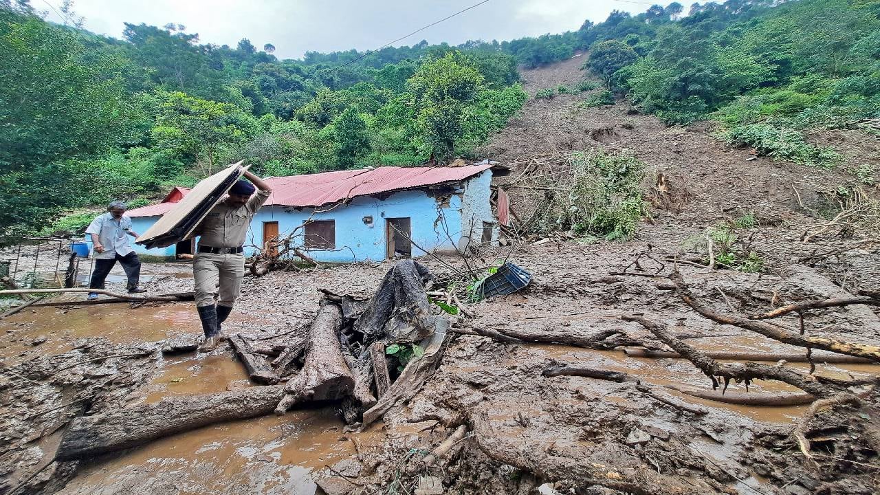 Un personal de seguridad lleva las pertenencias de un aldeano desde el lugar de un deslizamiento de tierra después de fuertes lluvias en India.