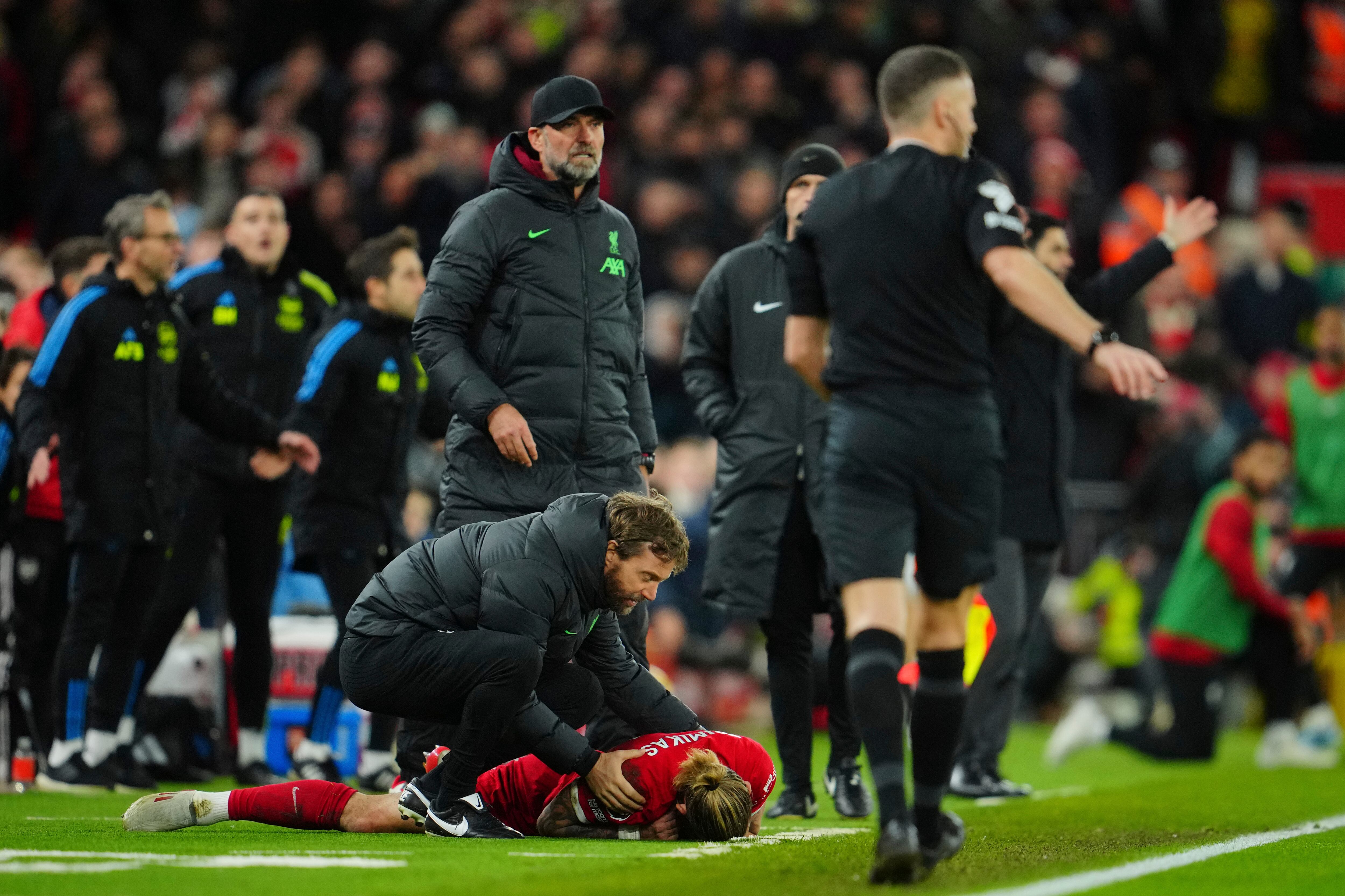 Liverpool's Kostas Tsimikas, bottom, grimaces in pain after a tackle by Arsenal's Bukayo Saka during the English Premier League soccer match between Liverpool and Arsenal at Anfield stadium in Liverpool, England, Saturday, Dec. 23, 2023. (AP Photo/Jon Super)
