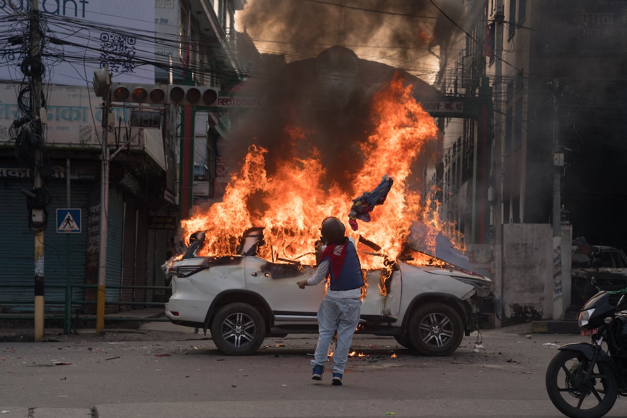 Un manifestante envuelto en la bandera nacional de Nepal prende fuego a un vehículo del gobierno en Mahendrapool en Pokhara, Nepal, el 9 de septiembre de 2025, durante una manifestación encabezada por la Generación Z contra la prohibición del gobierno de las redes sociales, mientras presiona por oportunidades de empleo, buena gobernanza y libertad de expresión. (Foto de Yunish Gurung/NurPhoto) (Foto de Yunish Gurung/NurPhoto vía AFP)