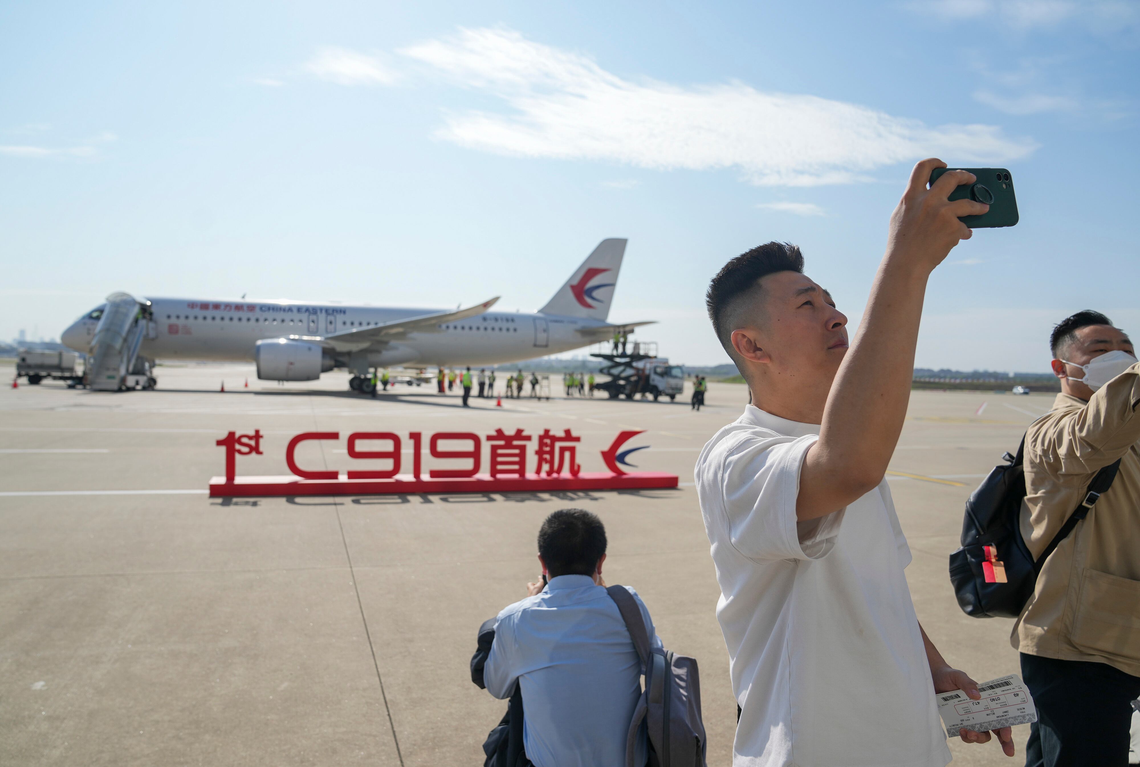 un pasajero se toma una selfie cerca de un letrero que dice "Primer vuelo inaugural C919" que se muestra frente al avión de pasajeros fabricado en China preparado para su primer vuelo comercial desde Shanghái el domingo 28 de mayo de 2023.