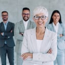 Portrait of beautiful smiling businesswoman with her colleagues. Multi-ethnic group of business persons standing together in modern office. Successful team leader and her team in background.