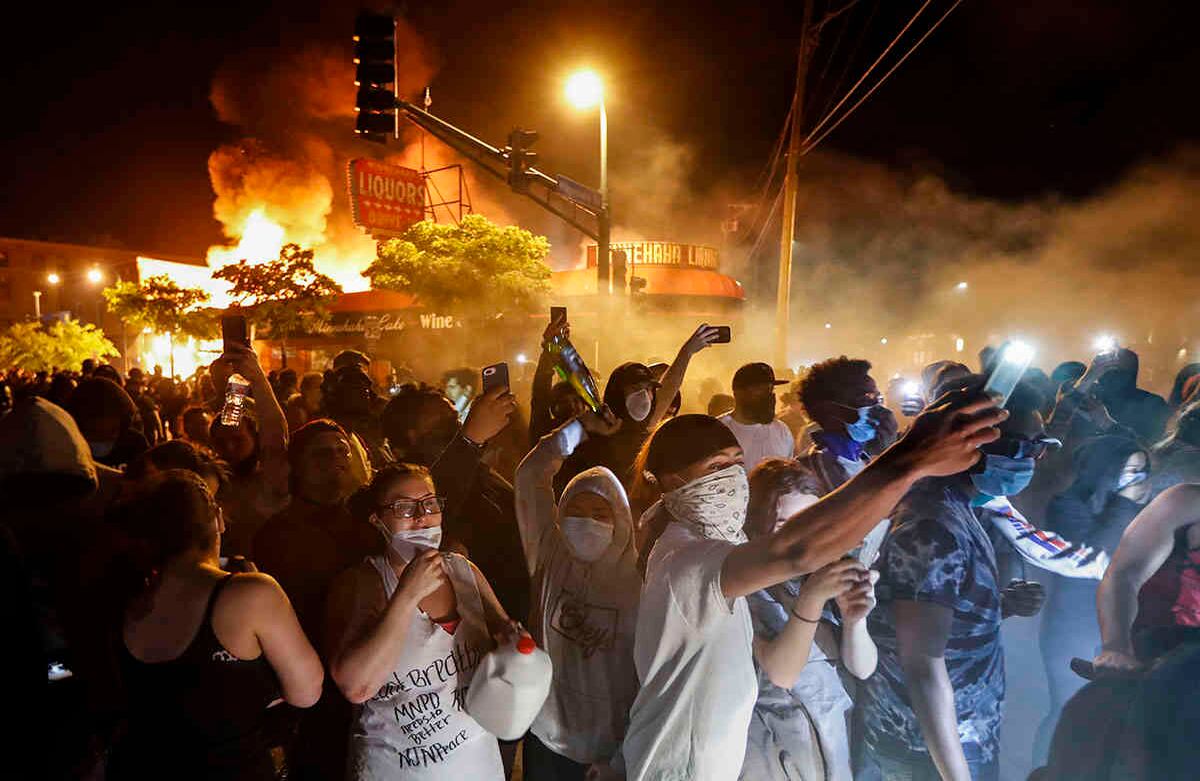 Una multitud protesta afuera de una tienda de licores en llamas cerca del tercer recinto policial de Minneapolis, el jueves 28 de mayo de 2020 (Foto AP / John Minchillo)