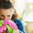 unhappy young female in orange apron and pink rubber gloves with mop in the modern living room in sunny day.