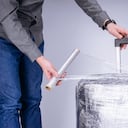 El hombre envuelve la película protectora transparente de la maleta (Imagen de referencia)