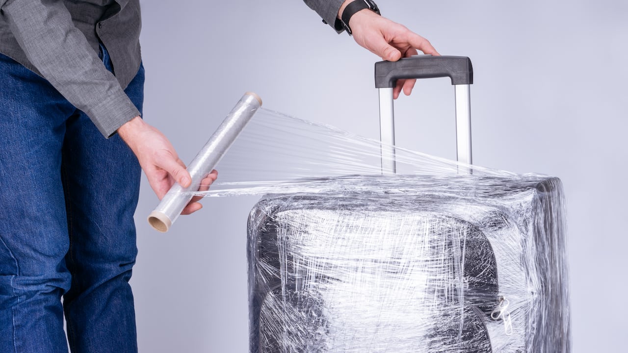 El hombre envuelve la película protectora transparente de la maleta (Imagen de referencia)