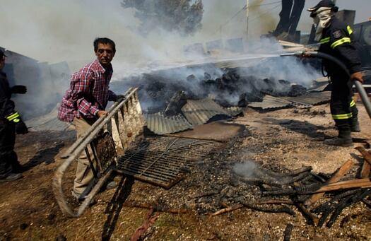 Un hombre salva sus pertenencia al mismo tiempo que los combatientes de fuego riegan su yarda en Dioni, al este de Atenas, Grecia.
