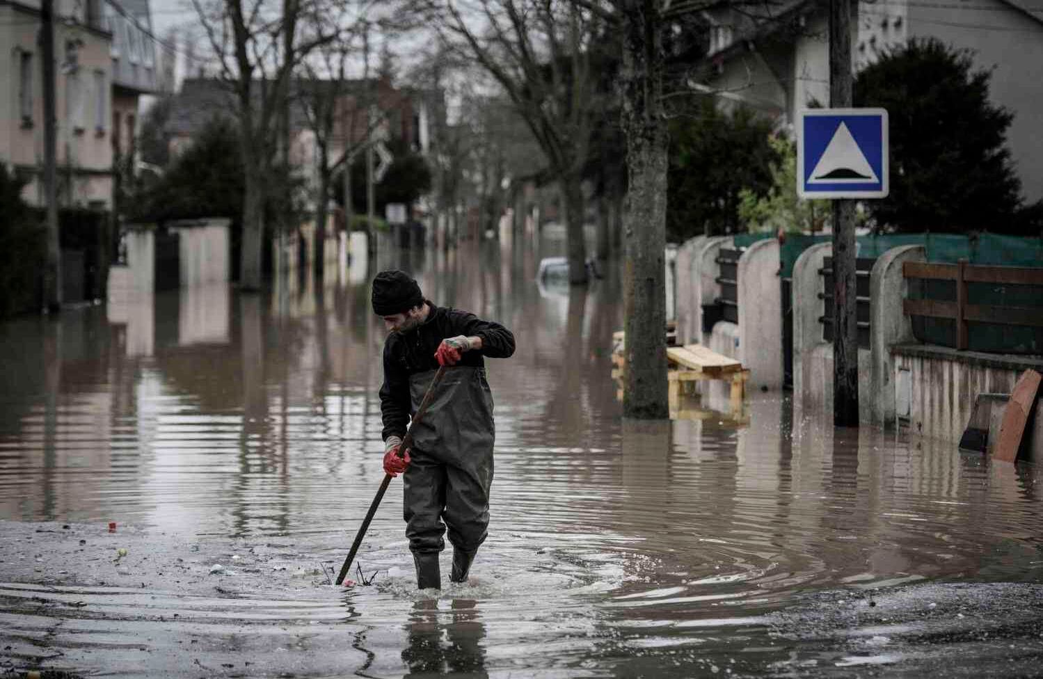 Un residente limpia los escombros de una calle inundada en Villeneuve-Saint-Georges, al sur de París, el 25 de enero de 2018. / AFP PHOTO / Philippe Lopez.