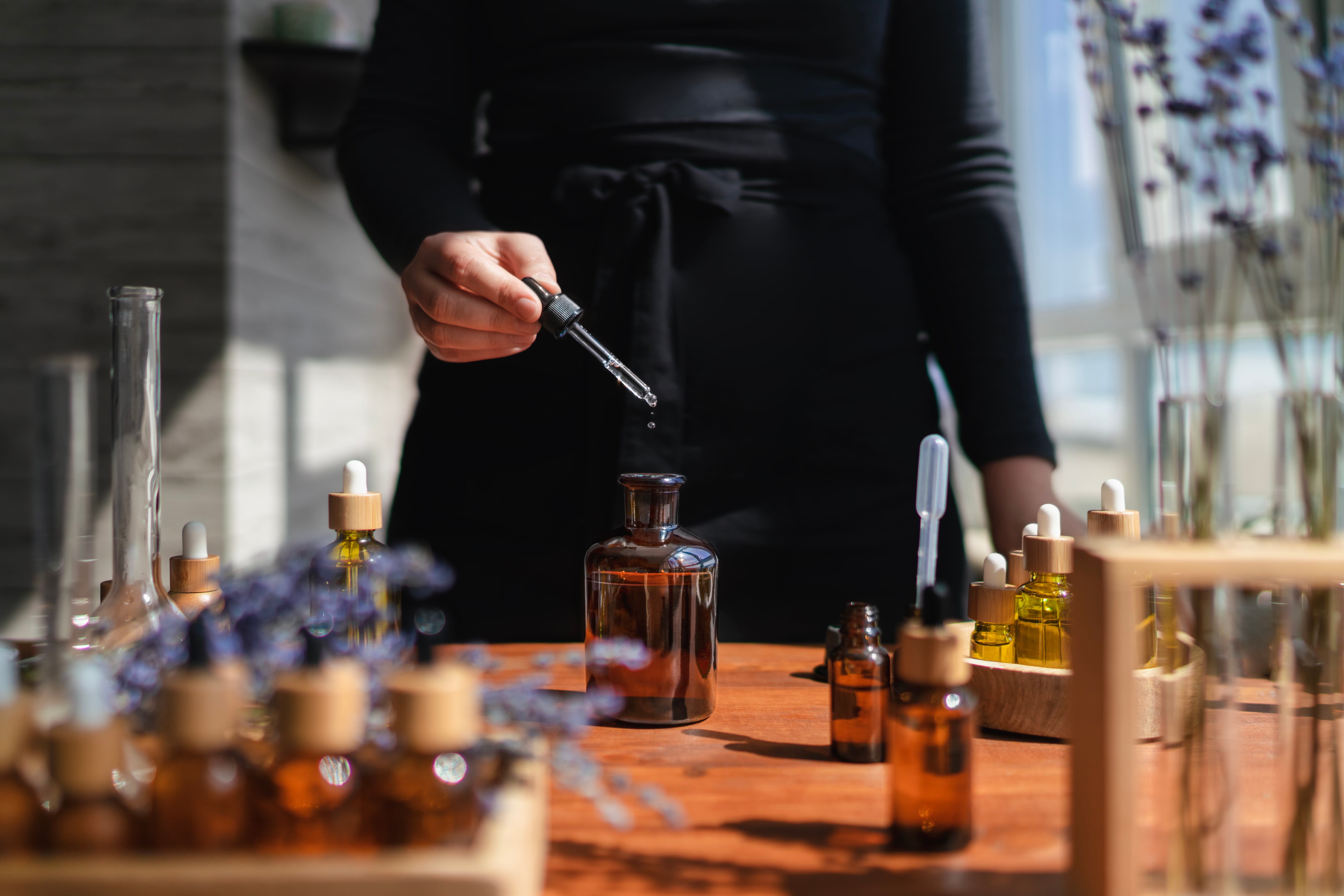 Mujer preparando líquido aromático para difusor o perfume a partir de aceite esencial de flores.