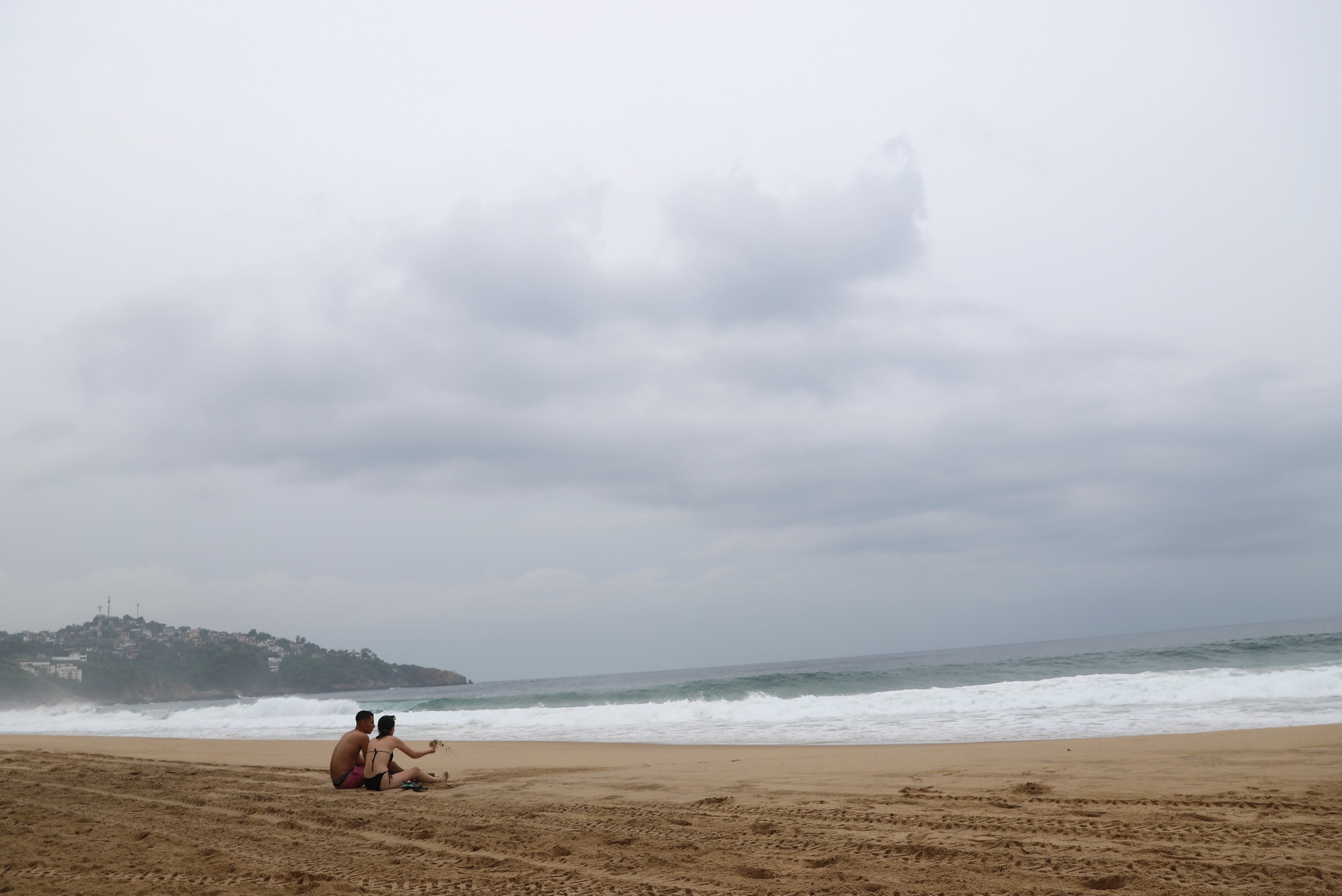 Turistas se sientan en la playa en Acapulco, México, el martes 24 de octubre de 2023. El huracán Otis se ha fortalecido de tormenta tropical a huracán de categoría mayor en cuestión de horas a medida que se acerca a la costa del Pacífico sur de México, donde se pronosticaba que tocaría tierra cerca del centro turístico de Acapulco temprano el miércoles. (Foto de AP/Bernardino Hernández)