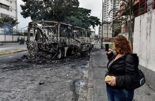 Una mujer le toma una foto a un bus incinerado en Caracas, minutos antes de que empiece la gran marcha de la oposición. Crédito: LUIS ROBAYO / AFP