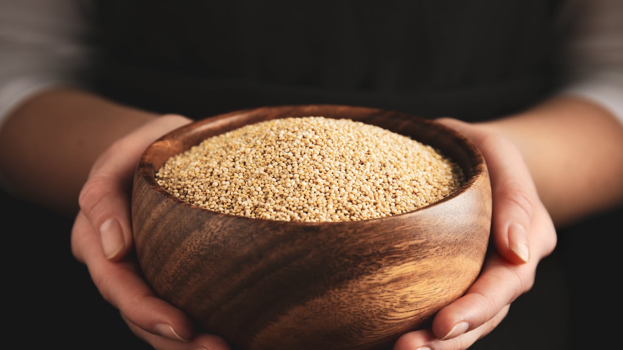 Woman holding wooden bowl with white quinoa on dark background, closeup