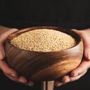 Woman holding wooden bowl with white quinoa on dark background, closeup