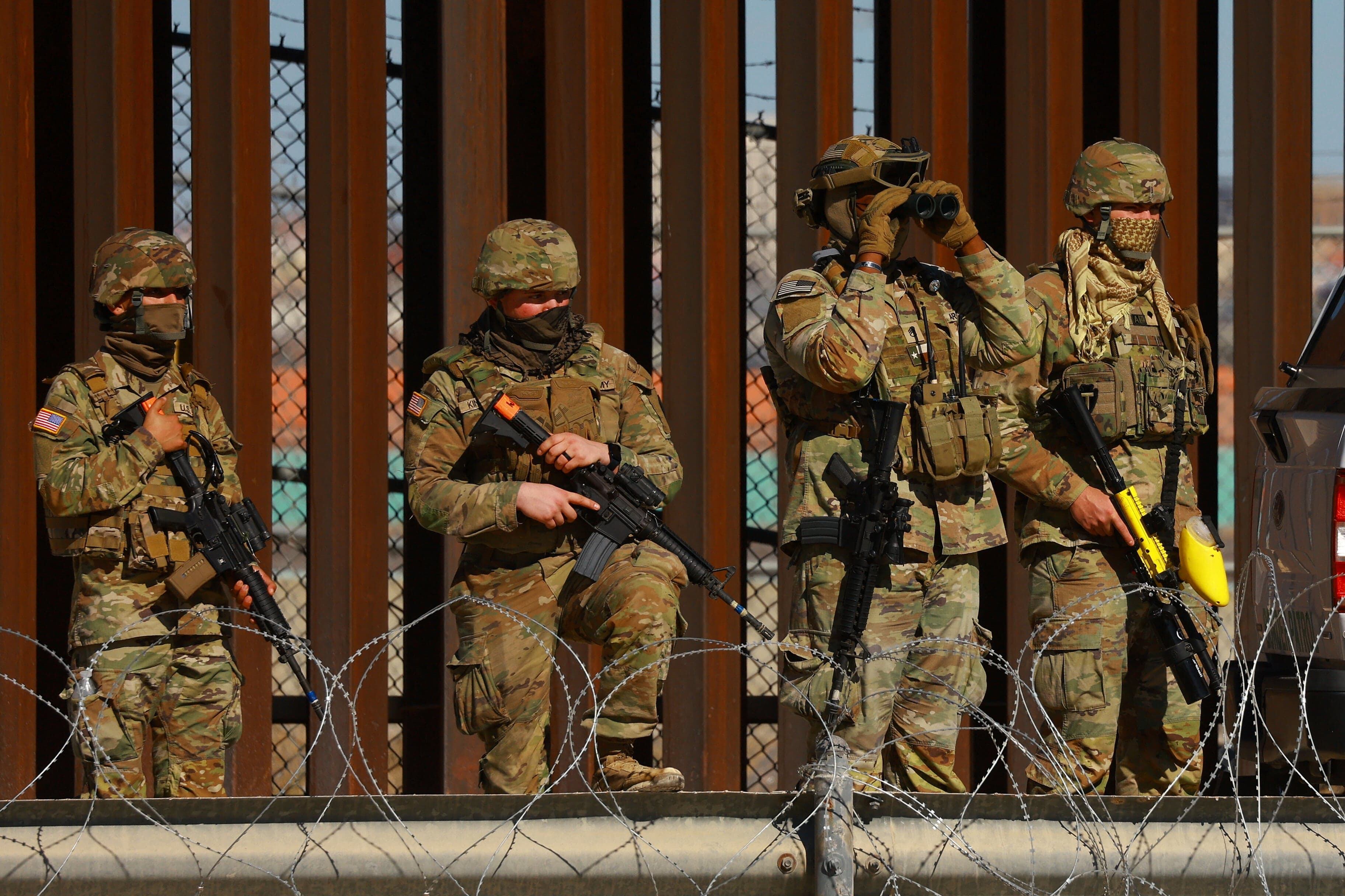 Guardias armados en uniforme observando el muro fronterizo desde un punto de control en el desierto de Texas.