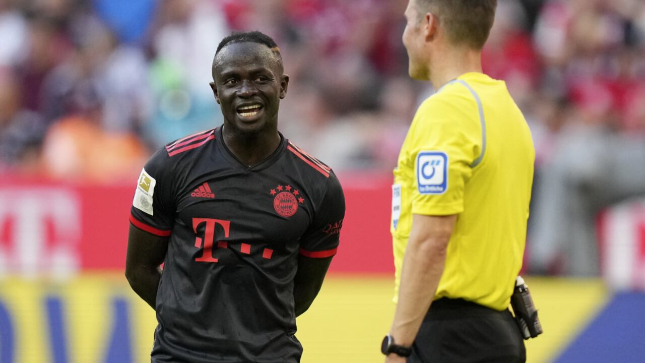 Sadio Mané del Bayern Múnich charla con el árbitro Harm Osmers a la espera de la decisión del VAR en el partido contra Wolfsburgo en la Bundesliga, el domingo 14 de agosto de 2022. (AP/Matthias Schrader)