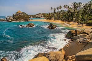 Hermosa playa tropical con el famoso monumento de una cabaña de playa y un océano azul con olas blancas, palmeras y bosque lluvioso en el Parque Nacional Tayrona, Colombia