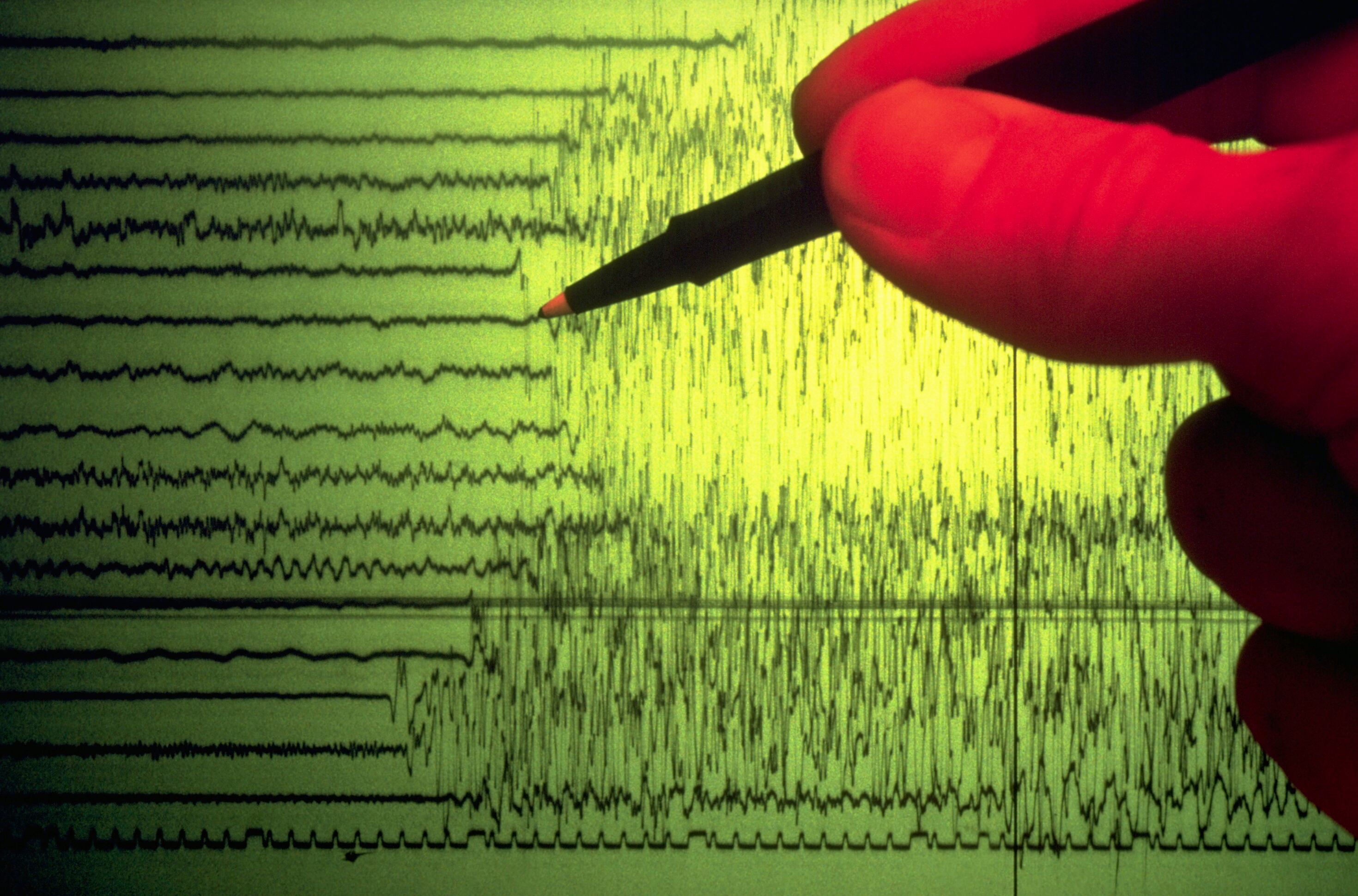 A seismographer uses a pen to point out the initial shock waves of an earthquake charted on a seismograph.
