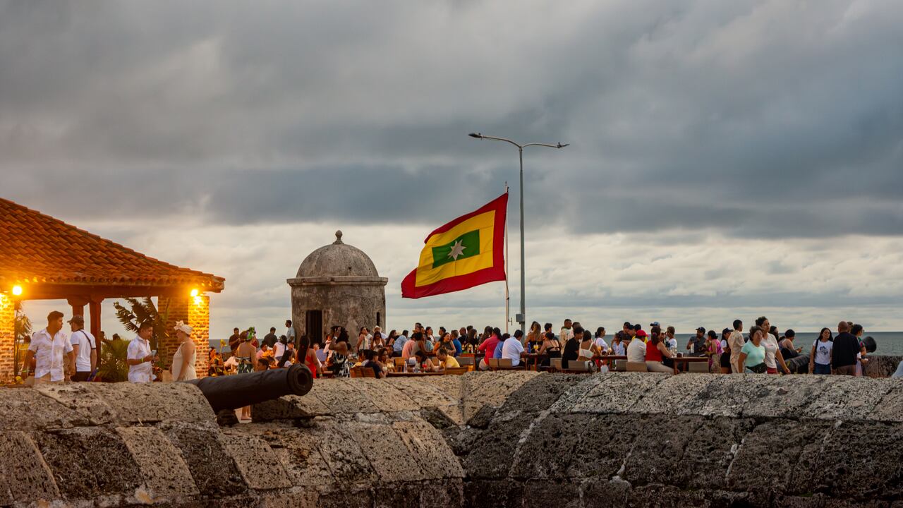 Cartagena, Colombia - 20 de agosto de 2025 - Una multitud animada disfruta de la vista panorámica con un cañón histórico y una bandera en primer plano.