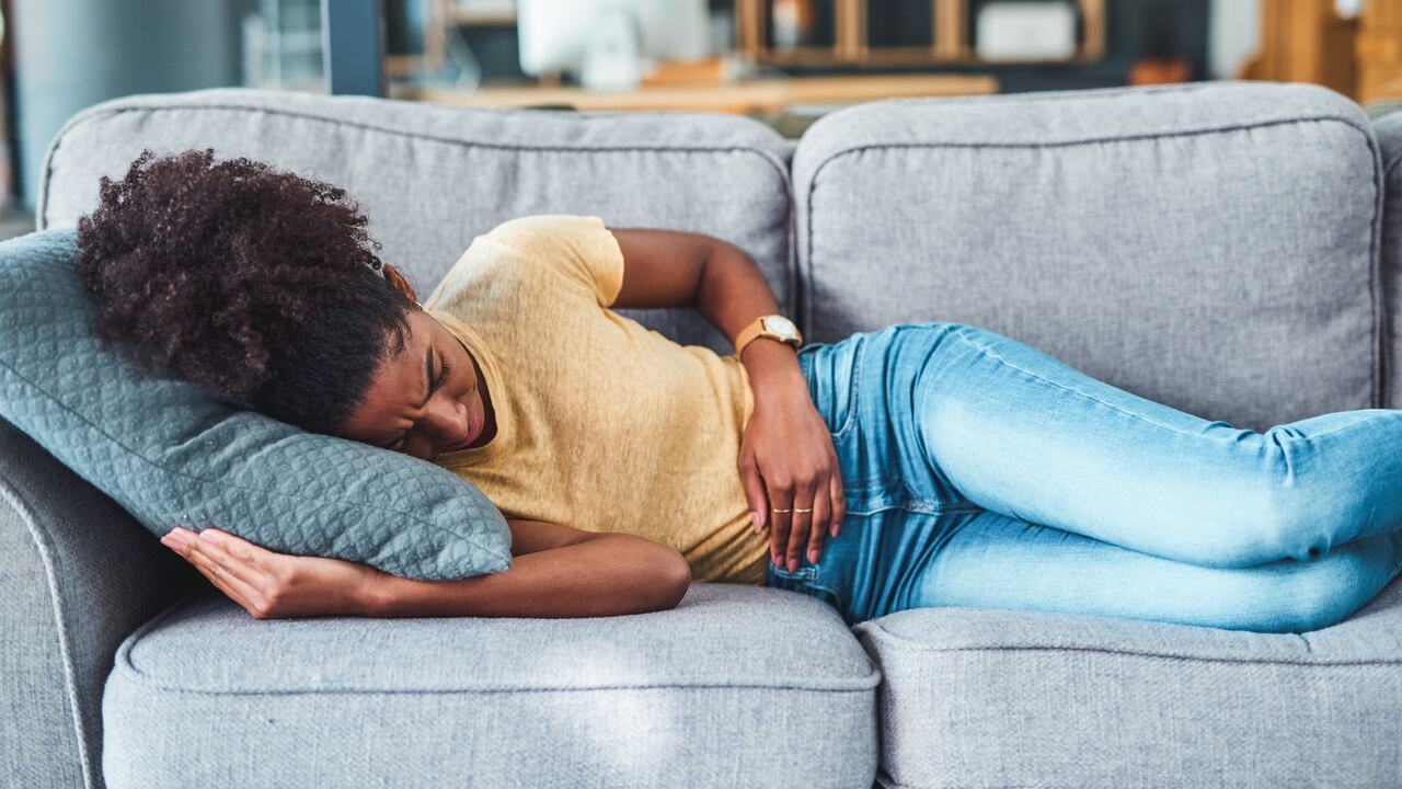 Shot of a young woman experiencing stomach pain while lying on the sofa at home
