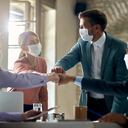 Grupo de colegas que usan tapabocas protectoras y juntan puños mientras tienen una reunión de negocios durante la pandemia de coronavirus.