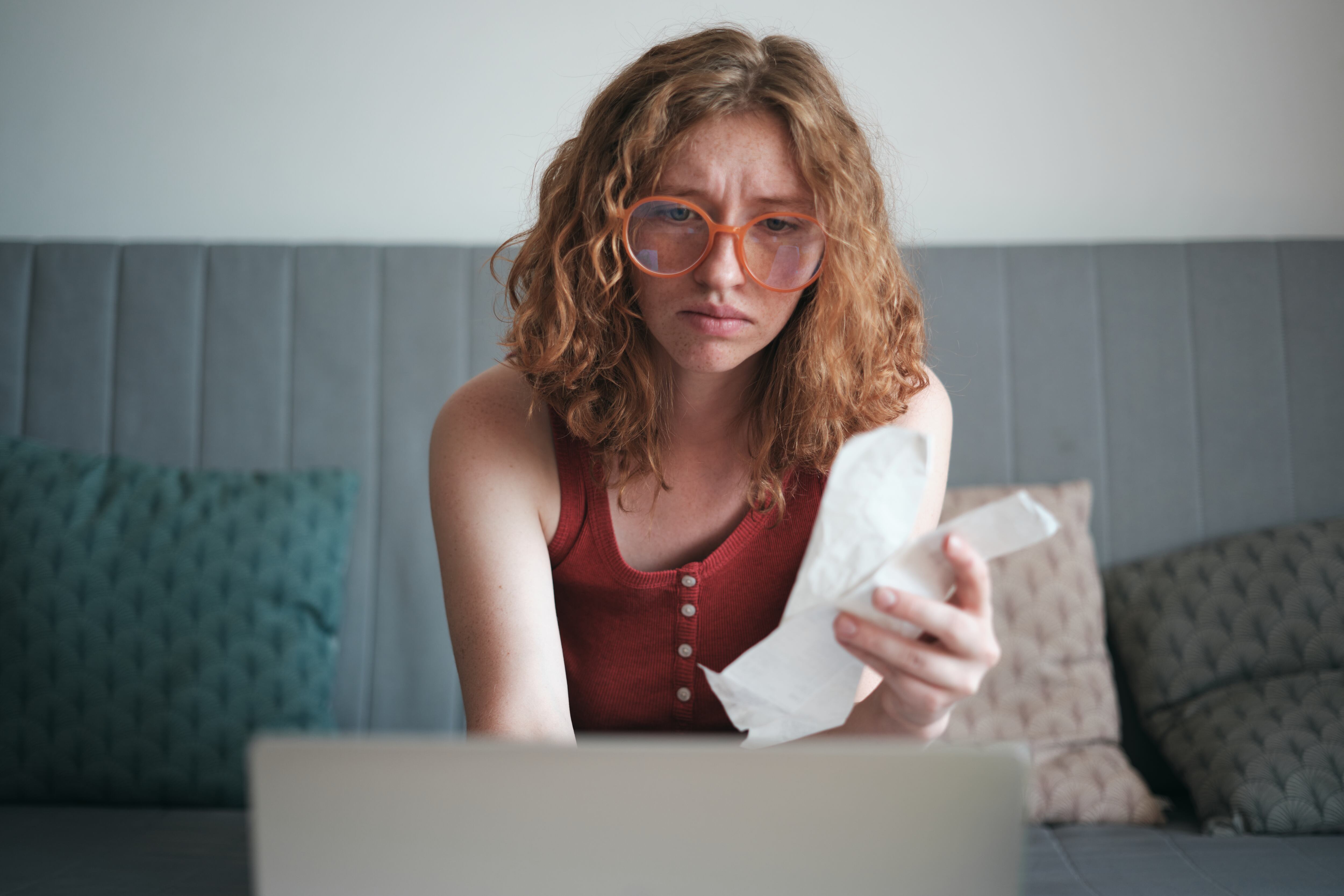 Chica de la Generación Z preocupada y triste con facturas y mirando la computadora portátil.