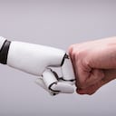 Robot y mano humana haciendo golpe de puño sobre fondo gris - Imagen de referencia