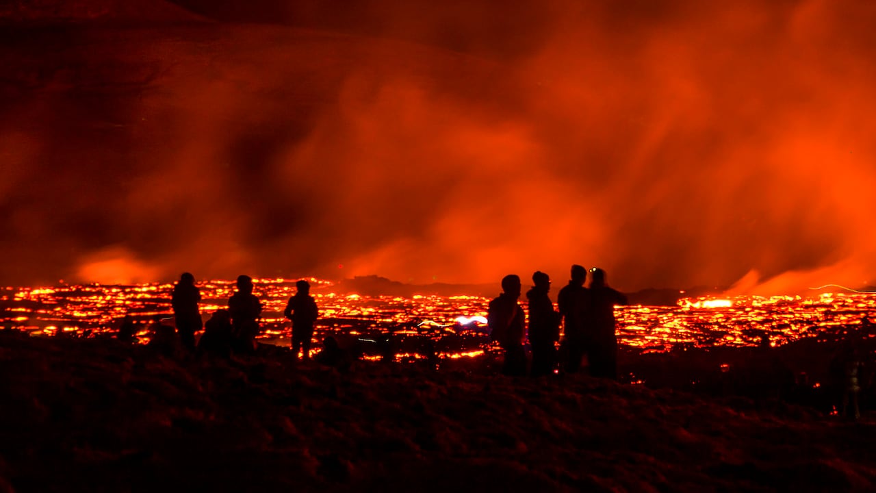 La gente observa cómo fluye lava de la erupción de un volcán en la península de Reykjanes en el suroeste de Islandia. La última erupción volcánica de Islandia atrae rápidamente a multitudes de personas que esperan acercarse a los suaves flujos de lava. Foto: AP / Marco Di Marco.