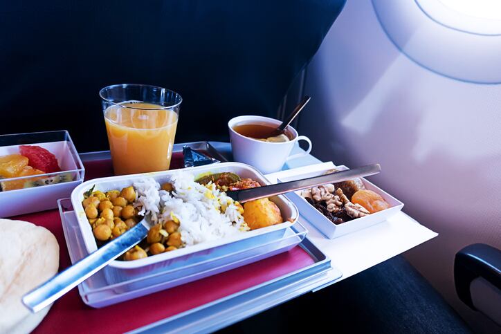 photo of Food served on board of economy class airplane on the table. set of Asian food. meals on the folding table in front of the aircraft window