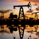 Pump jack silhouette against a sunset sky with reflections in the water.