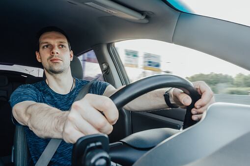 El joven conductor emocionado que sostiene un volante con las manos mira hacia adelante con curiosidad mientras conduce un automóvil a alta velocidad en la autopista. Un hombre con cinturón de seguridad en el interior de un vehículo.