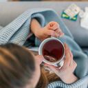 Vista superior de una mujer enferma con dolor de cabeza sentada en un sofá en casa envuelta en una manta durante el día. Enfermedad, concepto de problema de virus estacional. Mujer enferma con gripe acostada en el sofá.