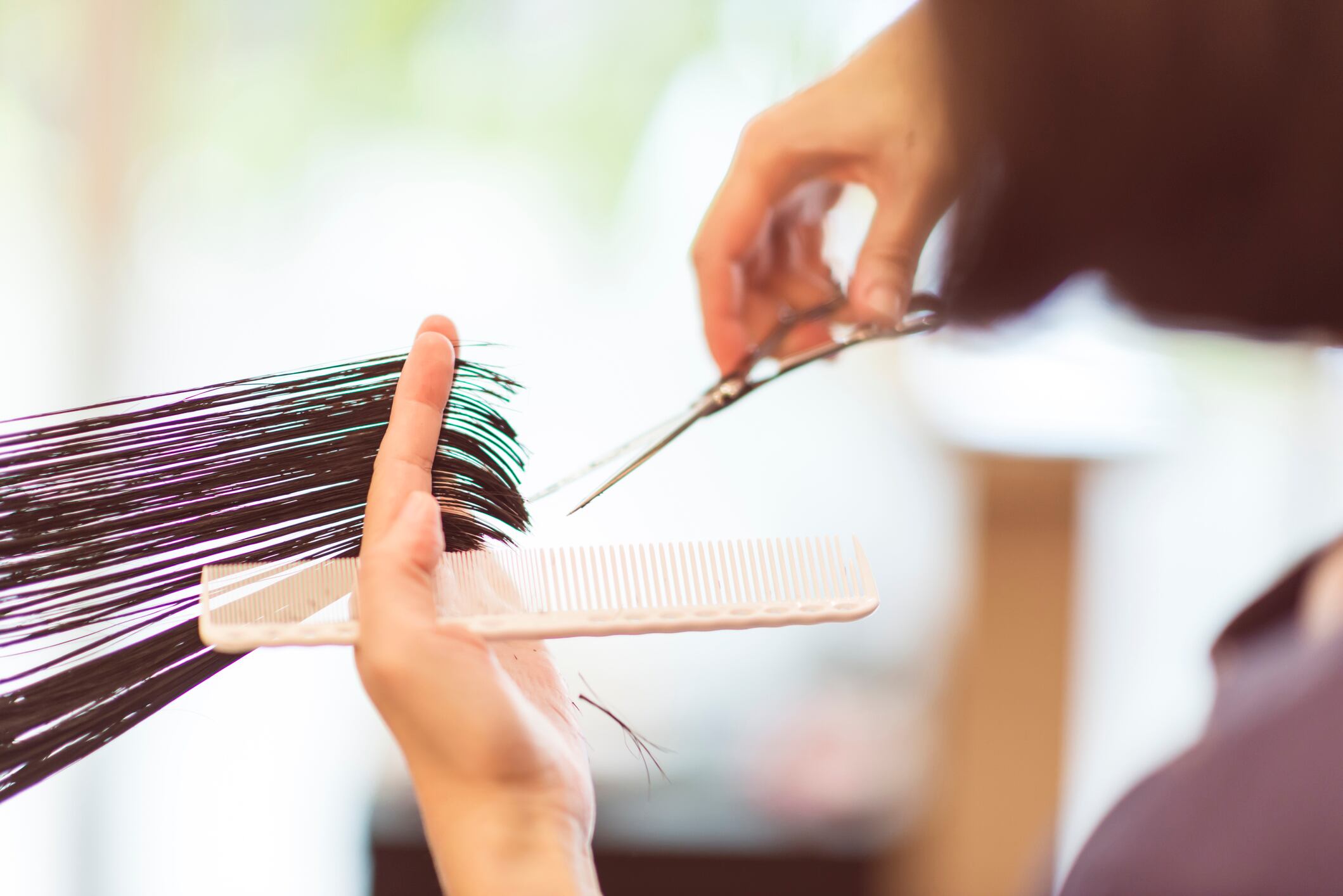 The hairdresser is cutting customer's hair with scissors and a comb
