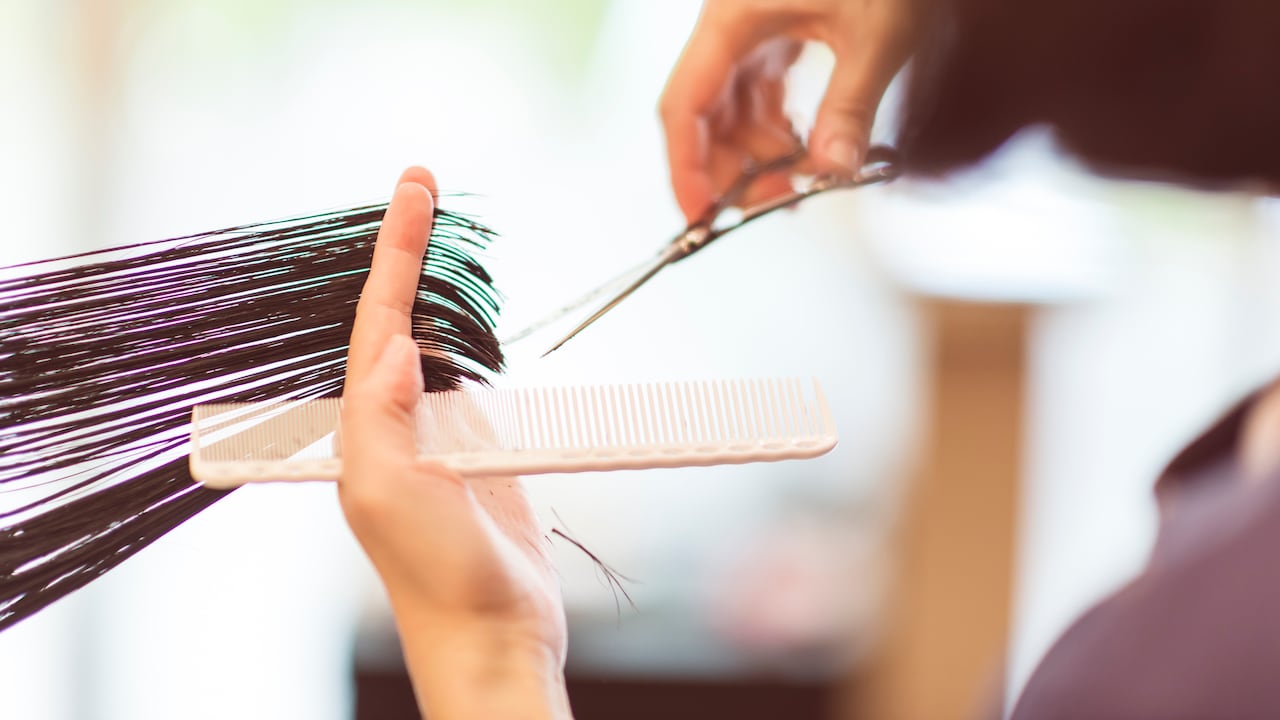 The hairdresser is cutting customer's hair with scissors and a comb