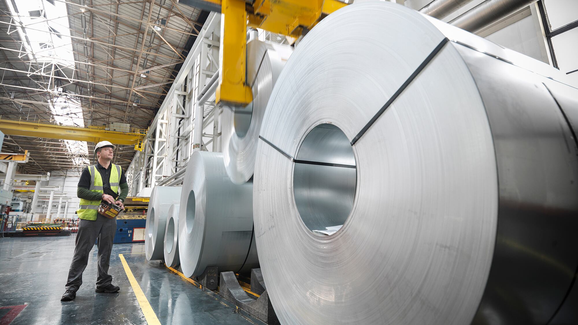 Worker operating crane with steel rolls in car factory