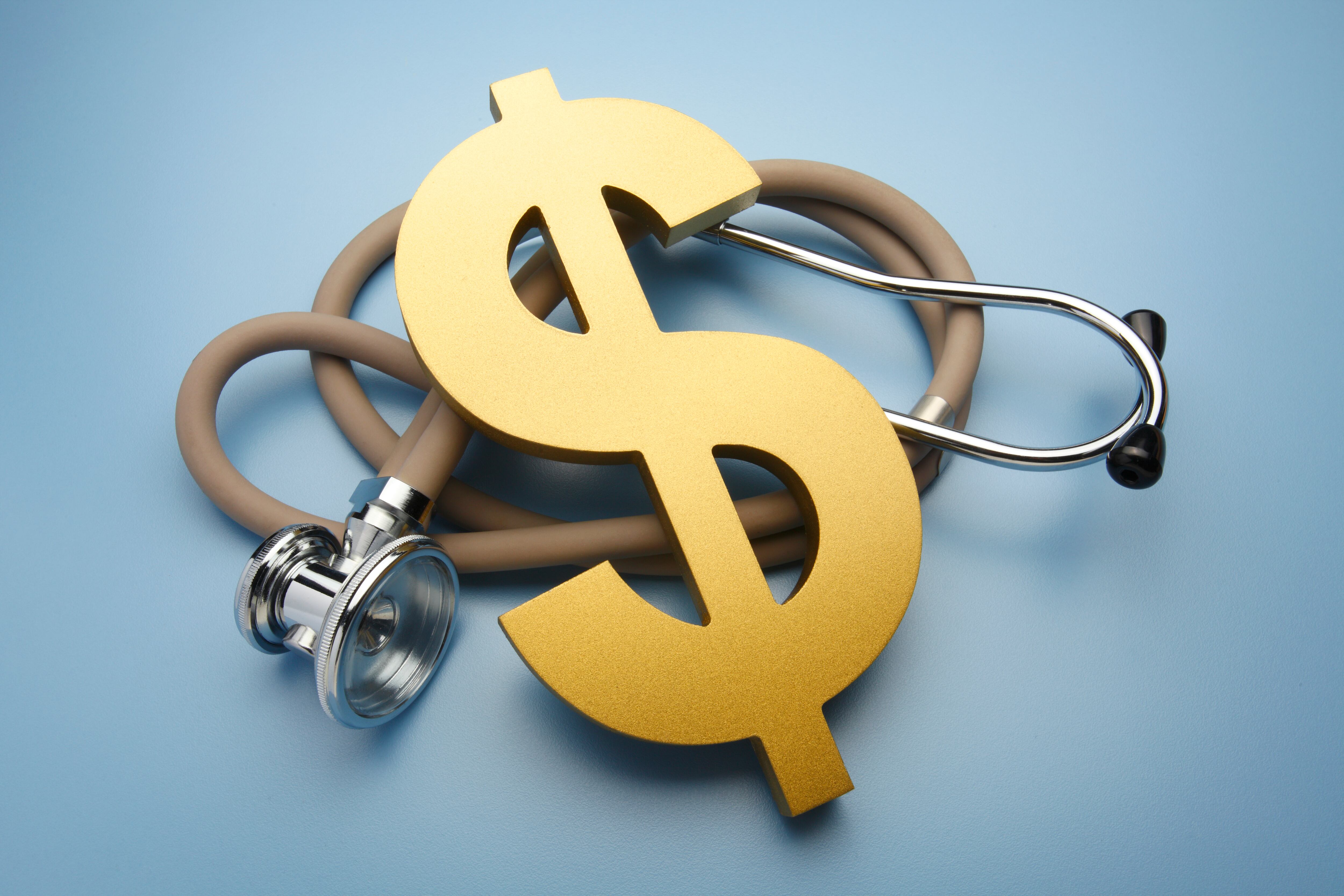 A large gold dollar sign rests on top of a stethoscope on a blue background representing the outrageous costs of health care and insurance.