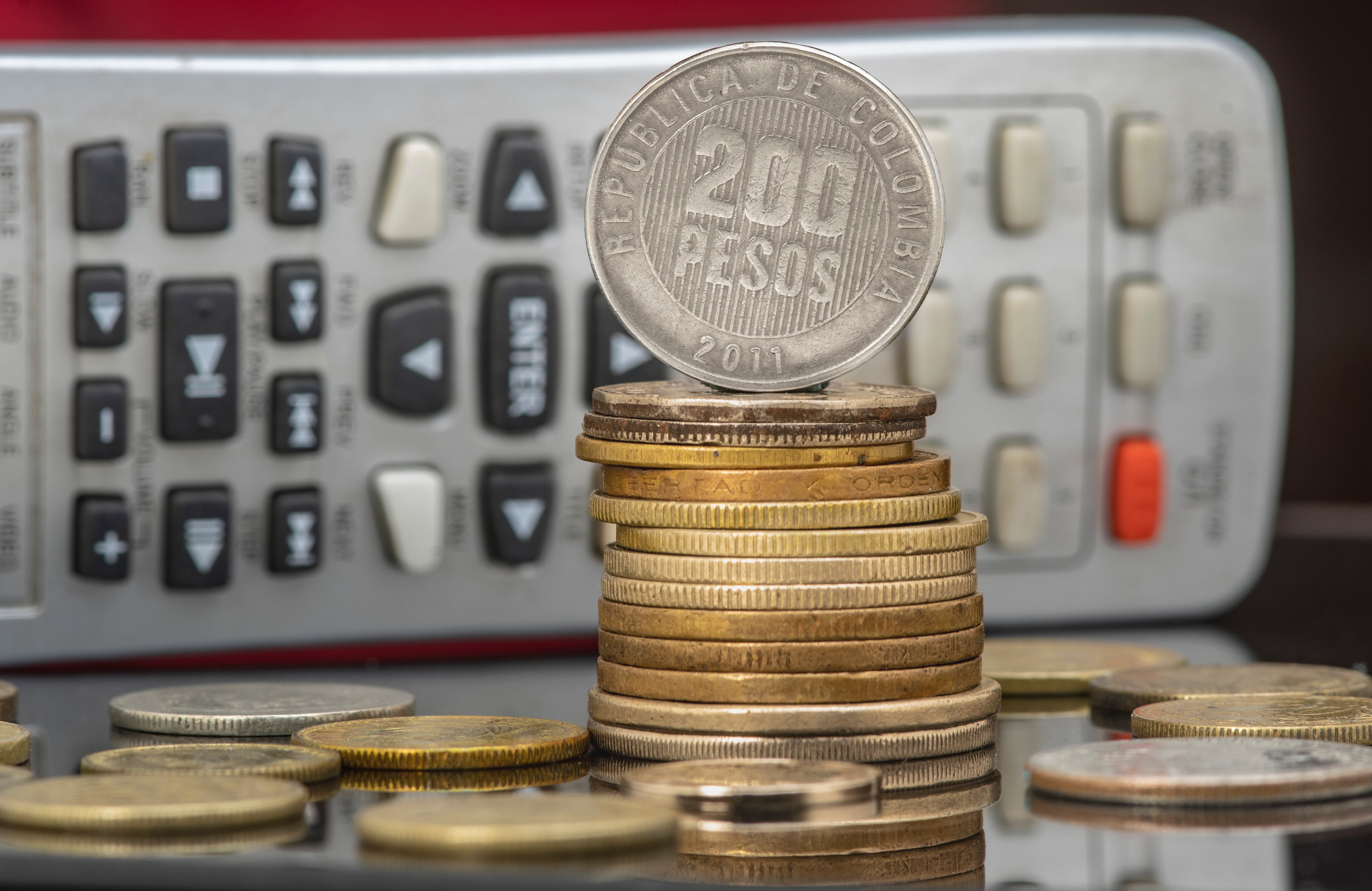 Pile and coins of Two Hundred Colombian Pesos with a calculator as a background. Income, expenses, taxes, financial data