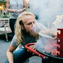 A young man is heating up the barbecue at a party by blowing on the coals.