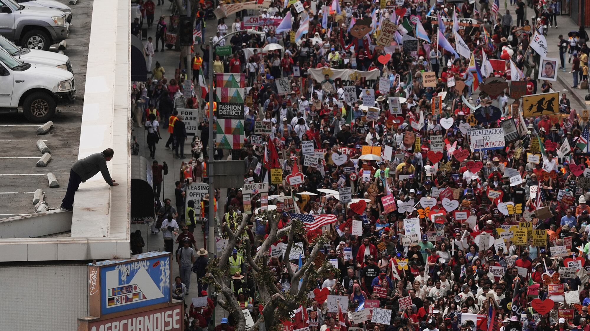 Un hombre se inclina sobre el borde de una estructura de estacionamiento para ver a los manifestantes marchar durante una protesta del primero de mayo en Los Ángeles, EE. UU. Jueves 1 de mayo de 2025.
