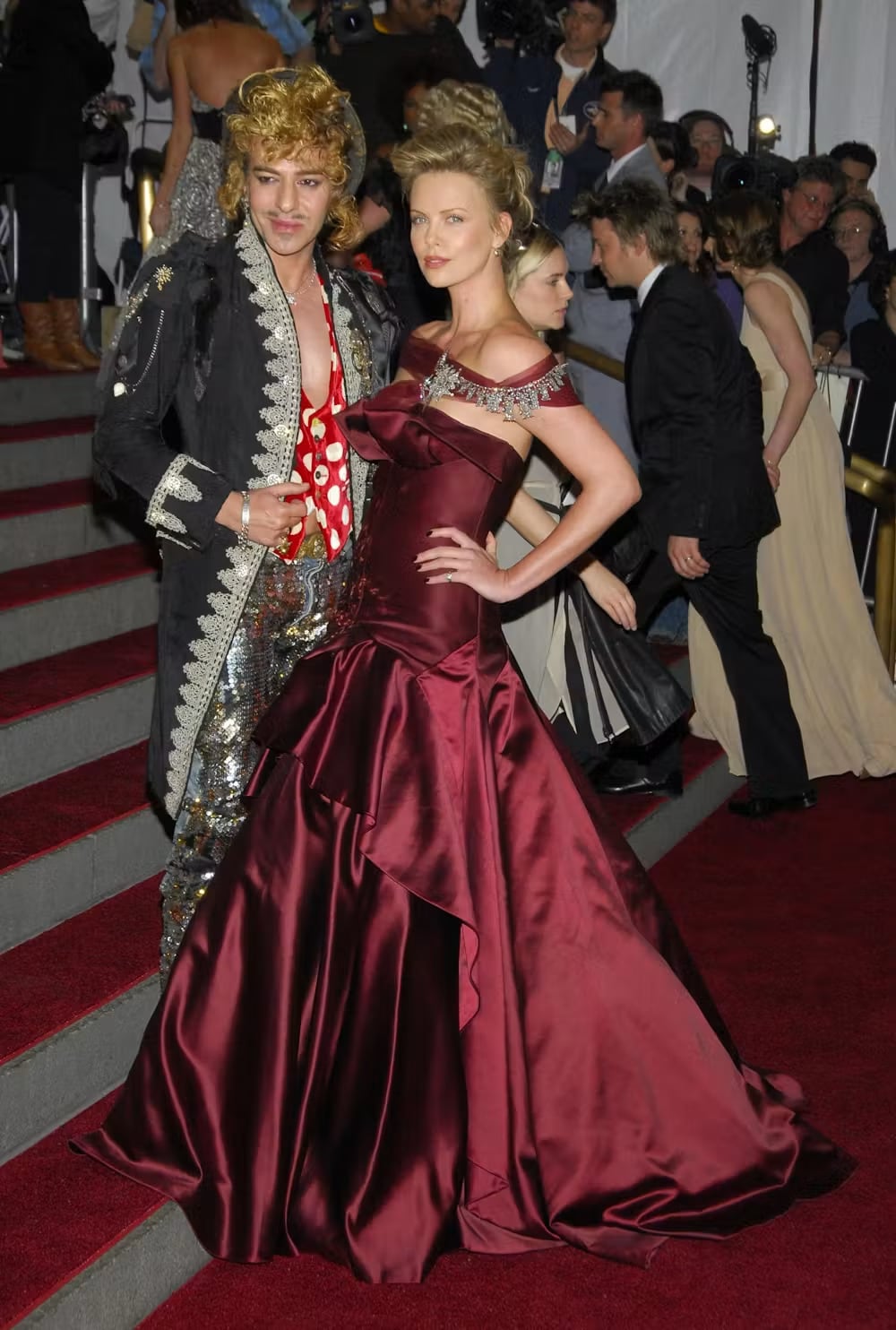 John Galliano y Charlize Theron, con un modelo de Dior Haute Couture diseñado por Galliano, en la gala inaugural de la exposición AngloMania: Tradición y transgresión en la moda británica, en el Museo Metropolitano, el 1 de mayo de 2006. Everett Colletion/Shutterstock